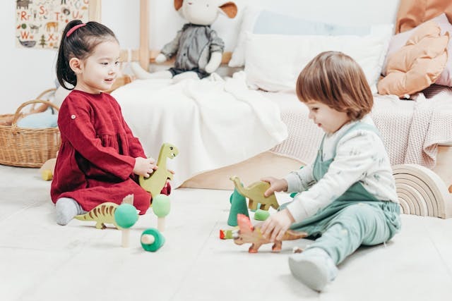 two young children seated playing with toy dinosaurs